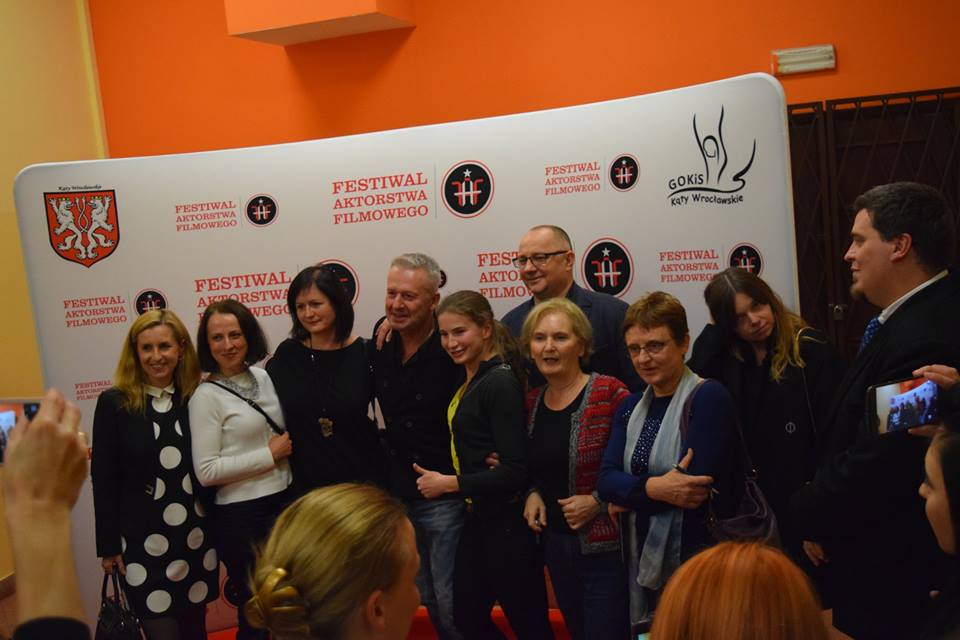 zdjęcie przedstawia grupe fanów z Bogusławem Lindą, wszyscy stoją na tle ścianki z logiem Festiwalu Aktorstwa Filmowego