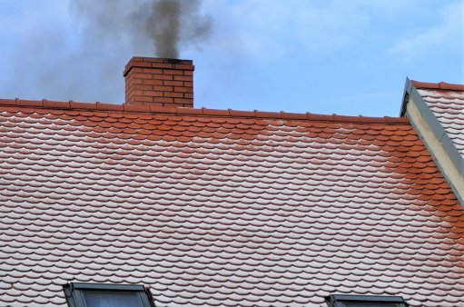 Na zdjęciu dach z kominem i czarnym dymem