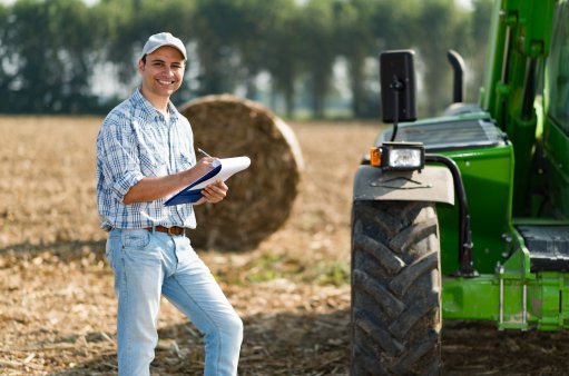 uśmiechnięty rolnik z dokumentami stoi na polu obok traktora