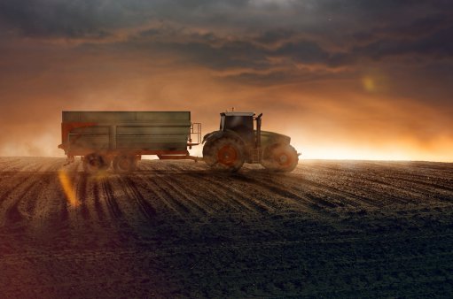 zdjęcie przedstawia traktor z przyczepą na tle zachodzącego słońca