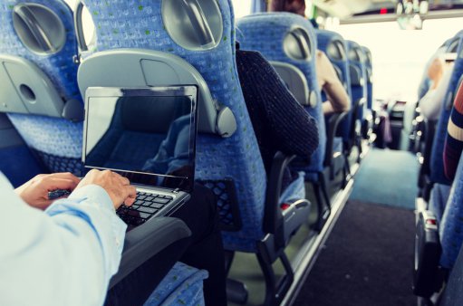 zdjęcie przedstawia wnętrze autobusu, po prawej stronie siedzi mężczyzna z laptopem na kolanach