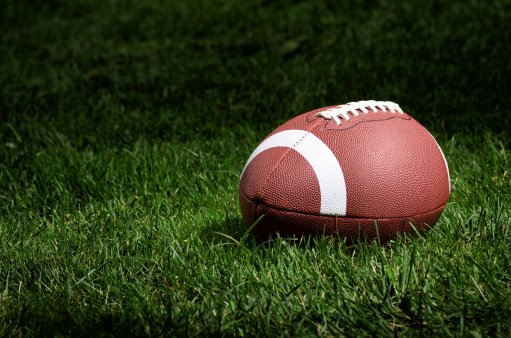 zdjęcie przedstawia piłkę do futbolu amerykańskiego leżącą na zielonej trawie