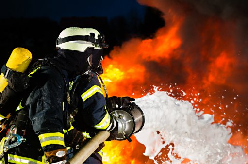 zdjęcie przedstawia dwóch strażaków trzymających sikawkę i gaszących ogień
