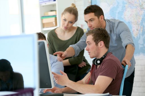 zdjęcie przedstawia troję młodych ludzi (2 mężczyzn i 1 kobietę), mężczyzna wskazuję ręką dwóm pozostałym osobom na ekran monitora